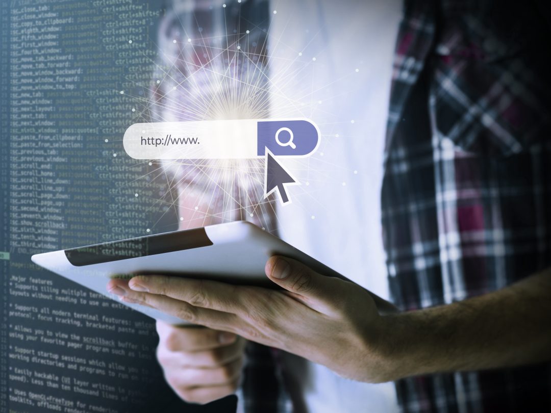 KI-Suche 2025 - Person hält ein Tablet mit eingeblendeter Suchleiste „http://www…“ und Lupen-Symbol; im Hintergrund Codezeilen – Symbolbild für und generative Webrecherche.