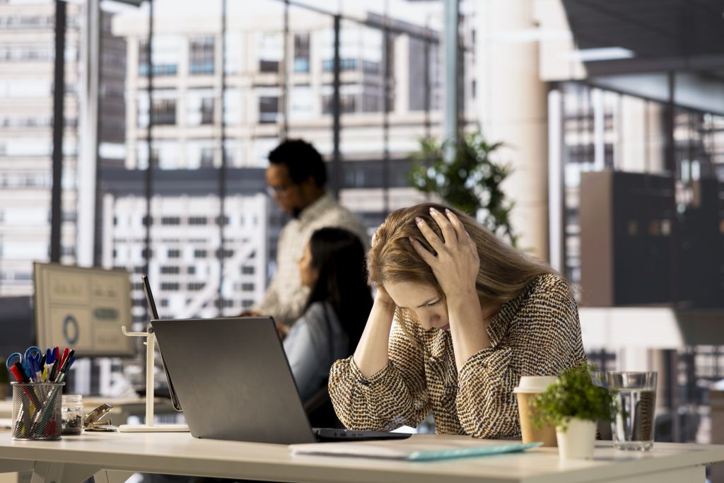 Gestresste Geschäftsfrau im Büro mit Kopfschmerzen vor Laptop – Stressmanagement im Berufsalltag