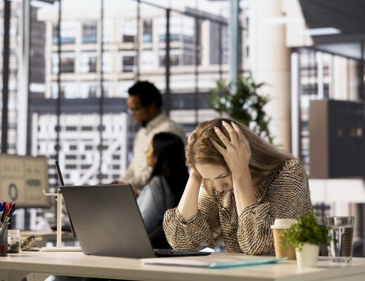 Gestresste Geschäftsfrau im Büro mit Kopfschmerzen vor Laptop – Stressmanagement im Berufsalltag