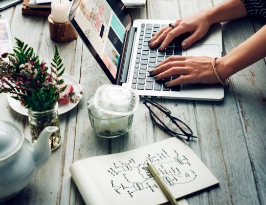 Eine Frau arbeitet am Laptop, umgeben von Notizen und einer Tasse Kaffee, während sie Online-Marketing-Trends recherchiert.