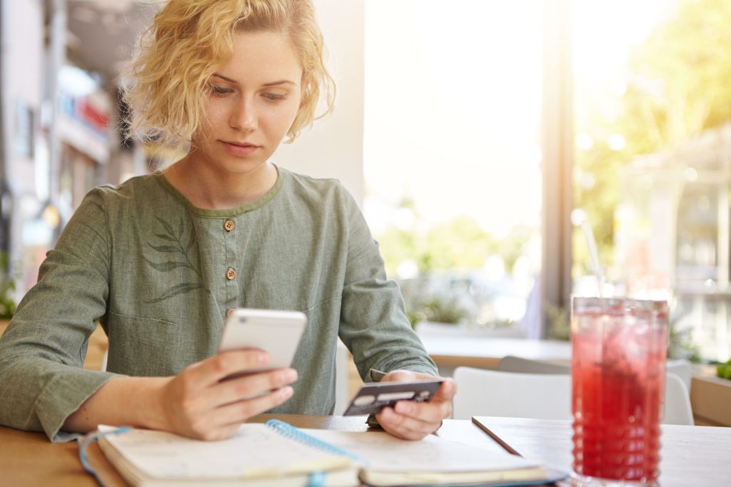 Frau nutzt ihr Smartphone, um einen Arzttermin online zu buchen und hält eine Bankkarte in der Hand.