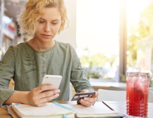 Frau nutzt ihr Smartphone, um einen Arzttermin online zu buchen und hält eine Bankkarte in der Hand.